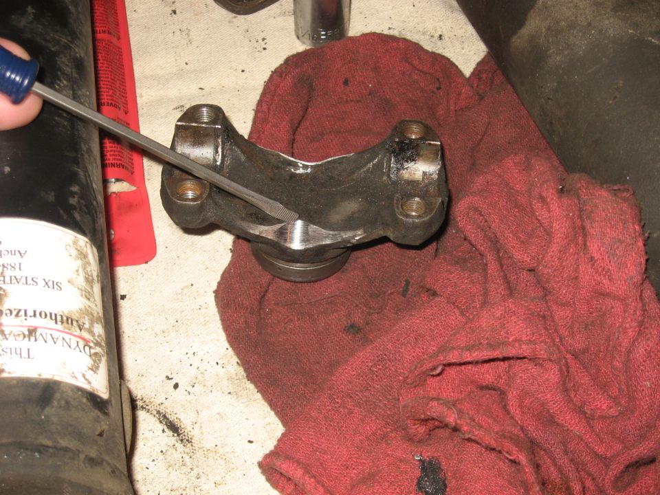 Driveshaft U-joint being filed with a blue-handled file, resting on a red shop rag