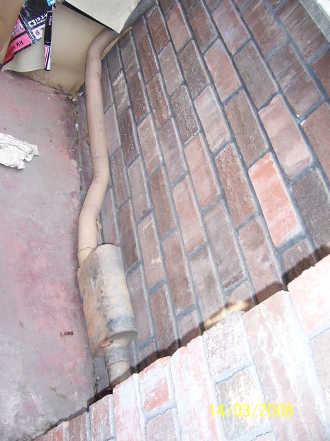 1991 Ford Bronco - Exhaust pipe and muffler are visible against a brick wall with some cardboard boxes above.