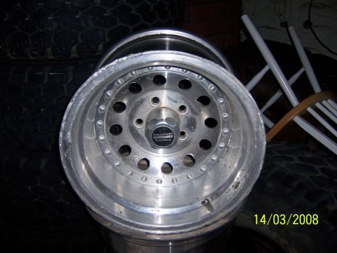 1991 Ford Bronco - A single aluminum wheel with the American Racing logo is shown, with tires stacked in the background.