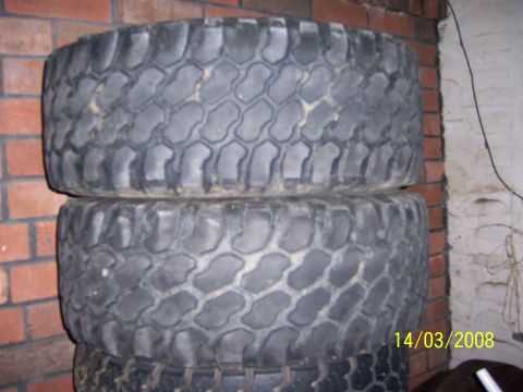 1991 Ford Bronco - Three off-road tires are stacked against a brick wall, showing their deep tread patterns.