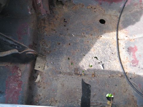 1988 Ford Bronco - The floor pan of a vehicle shows significant rust and corrosion, with visible holes and debris.