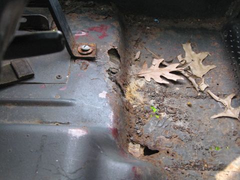 1988 Ford Bronco - Interior floor shows significant rust and damage, with leaves and dirt accumulated.