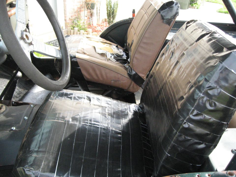 Vehicle interior with torn tan seats covered in black tape, and a dark steering wheel
