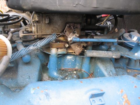 1988 Ford Bronco - Close-up view of an engine's carburetor and associated linkage, with a blue painted manifold visible.