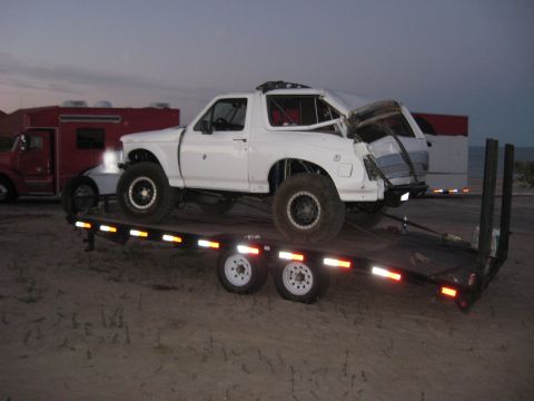 1994 Ford Bronco - Modified white Ford Bronco loaded onto a trailer, with a red truck visible in the background.