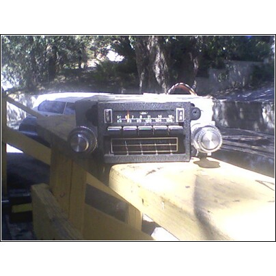 1973 Ford Ranchero - An 8-track player with push buttons and knobs is displayed on a wooden surface, with trees in the background.