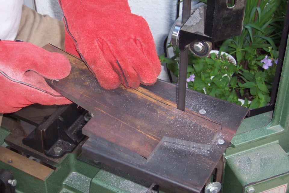 Metal bar with a notch being cut by a band saw, held by gloved hands