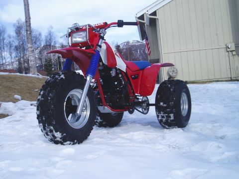 2000 Ford E350 - A red three-wheeled ATV sits in a snowy landscape next to a building.
