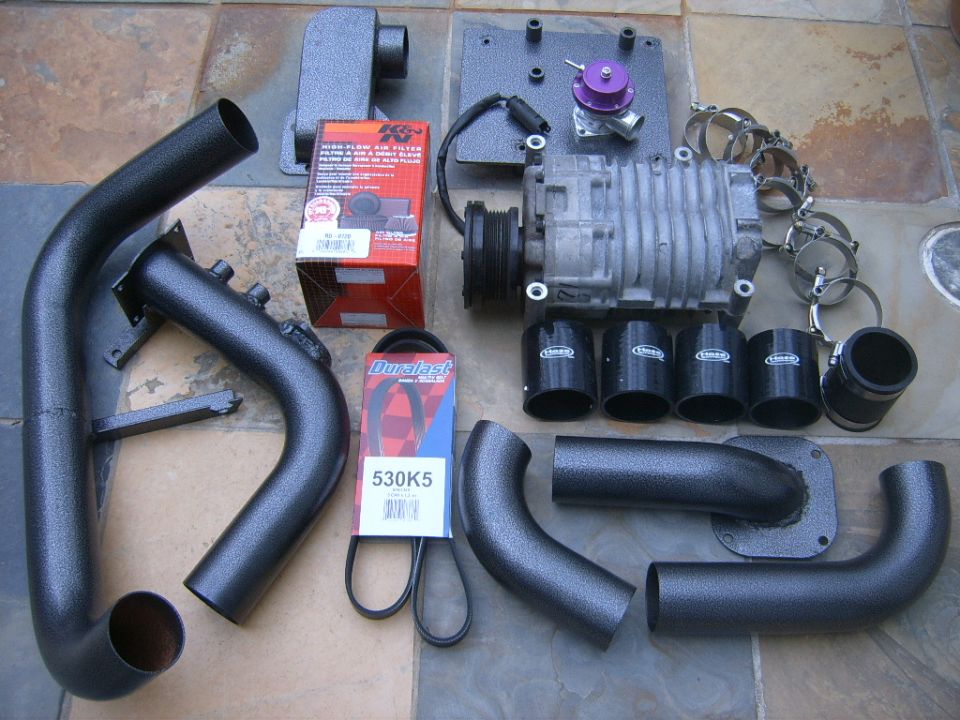 Supercharger kit with pipes, silicone couplers, clamps, K&N filter and belt on tiled floor.
