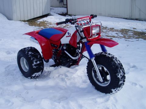 2000 Ford E350 - A red Honda three-wheeler sits in a snowy landscape, with a white section on the gas tank and blue suspension springs.