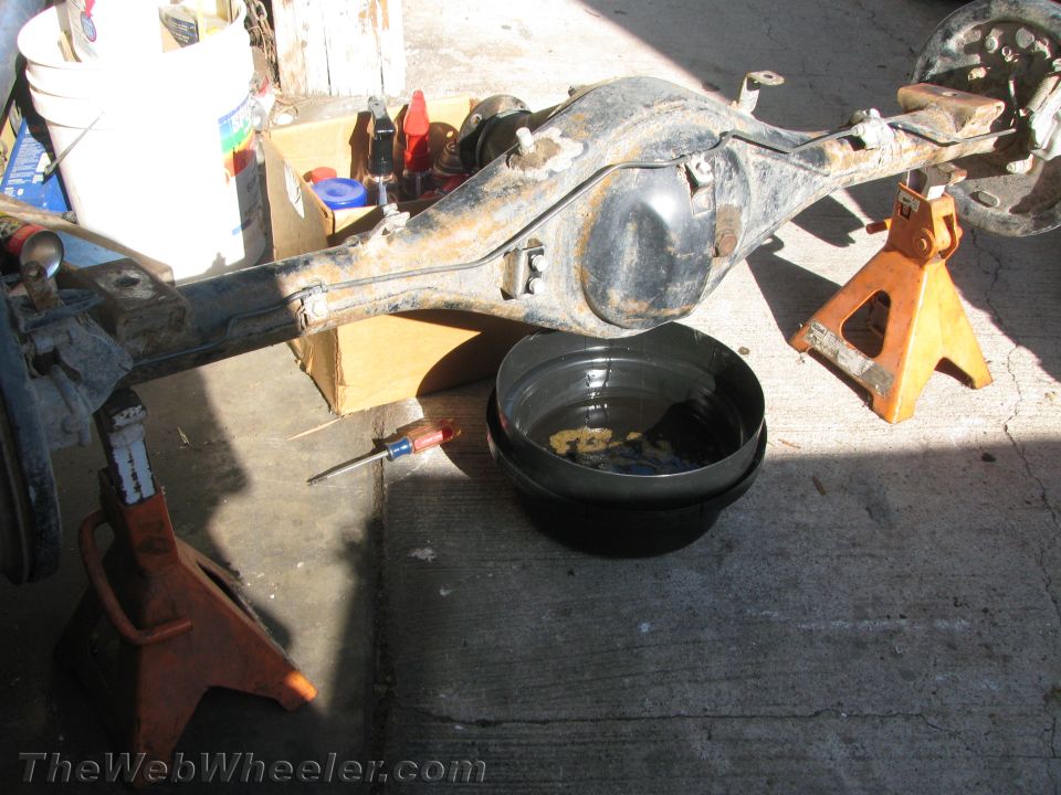 Rusty rear axle assembly on orange jack stands with a drain pan and screwdriver
