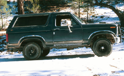 1980 Ford Bronco - This Ford Bronco is parked in a snowy, wooded landscape, showing its side profile and off-road tires.