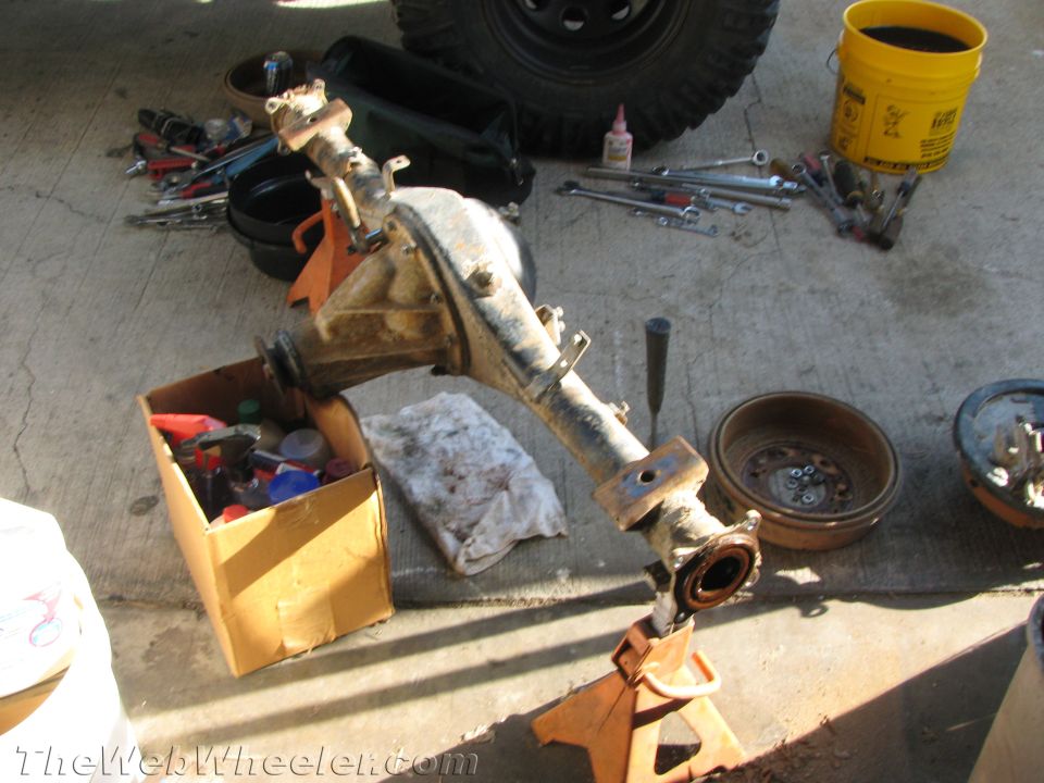 Vehicle axle assembly on jack stands with tools and parts scattered around