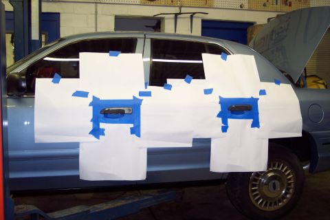 2001 Ford Crown Victoria - The door handles of a blue sedan are taped off, likely for painting or repair.