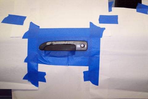 2001 Ford Crown Victoria - A car door handle is taped off with blue masking tape against a white background.