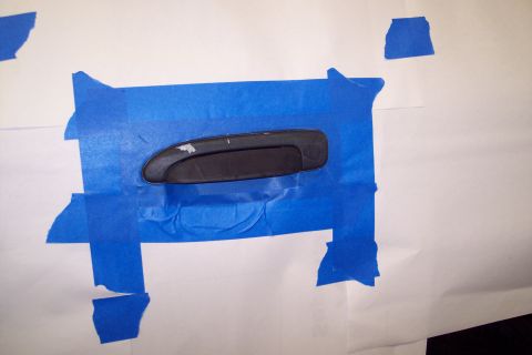 2001 Ford Crown Victoria - A black door handle is taped to a white surface with blue painter's tape.
