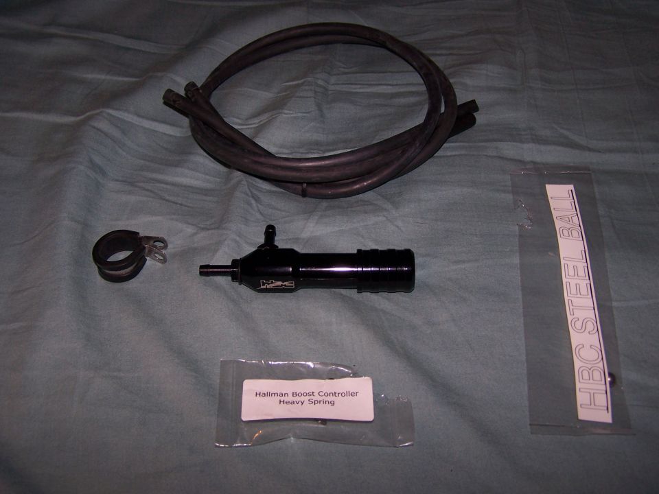 Hallman Boost Controller, heavy spring, two hoses, and a clamp laid out on a blue cloth. Includes a bag with text 'Hallman Boost Controller Heavy Spring'