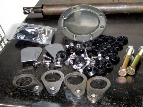 1996 Ford Bronco - Various vehicle hardware, including a fuel door and mounting components, are laid out on a workbench.