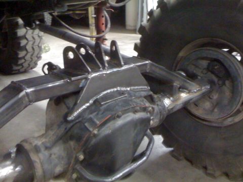 1966 Ford Bronco - Custom suspension mounts are welded onto the rear axle of a vehicle, with a large tire in view.