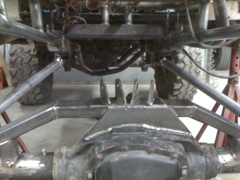 1966 Ford Bronco - Close-up view of a custom 4-link suspension system installed on a vehicle's rear axle, with large off-road tires in the background.