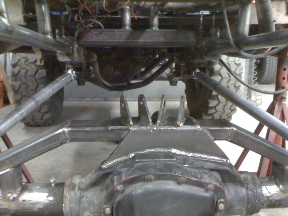 Welded link and shock brackets on a solid axle housing under a truck in a shop