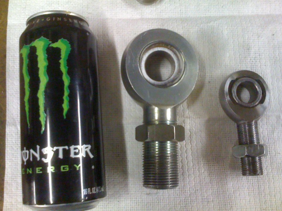 Large and small steel heim joints with jam nuts next to a Monster can for scale