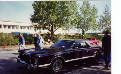 1998 Ford Crown Victoria - A vintage coupe with a vinyl roof is parked next to a building, with a red car in the background.