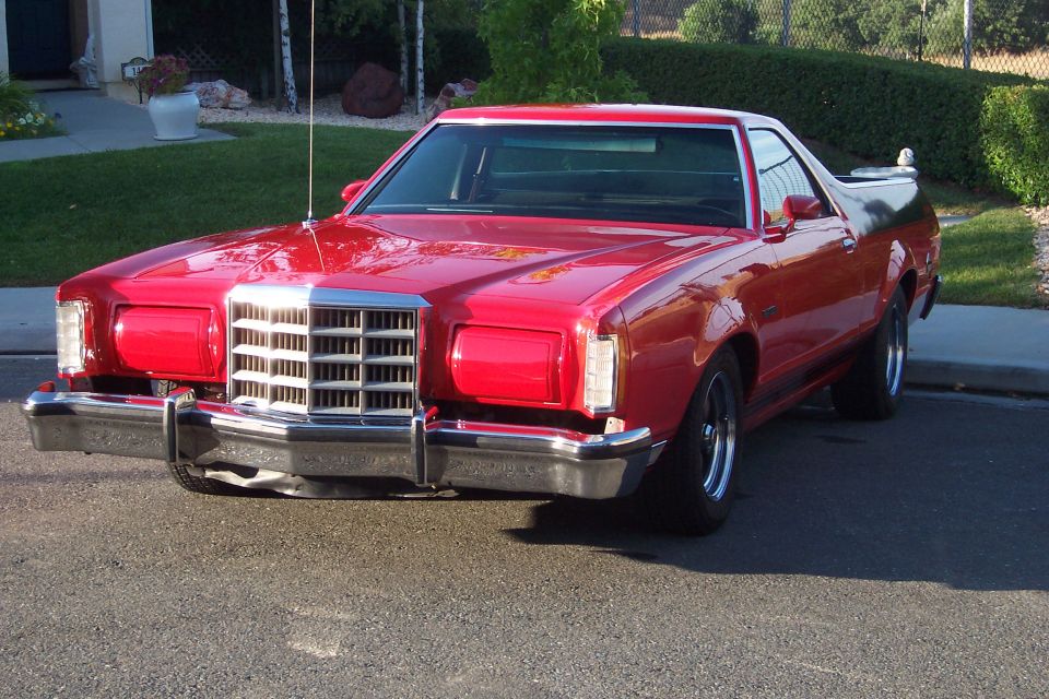 Red 1977 Ford Ranchero with a chrome grille and black bed cover, parked on asphalt