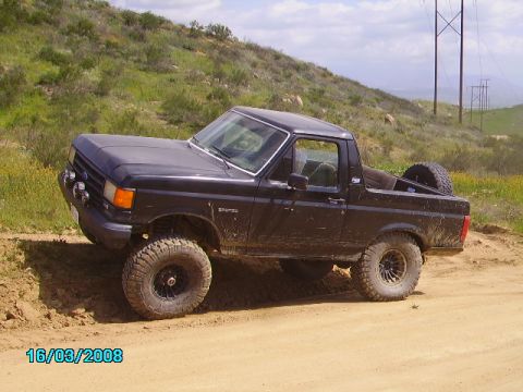 1990 Ford Bronco - This 1990 Ford Bronco is shown off-road on a dirt path with hills in the background.