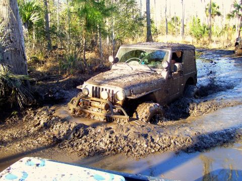 2004 Jeep TJ - A 2004 Jeep TJ navigates a challenging muddy off-road course, with another vehicle visible in the background.