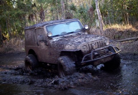 2004 Jeep TJ - A Jeep Wrangler is shown off-roading through a muddy, wooded area.