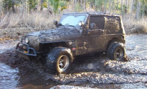 2004 Jeep TJ - This Jeep Wrangler is navigating a challenging off-road course covered in mud.