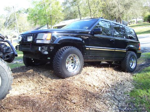 2004 Jeep TJ - A black Jeep Grand Cherokee, modified with a new bumper and off-road tires, sits on a dirt lot.