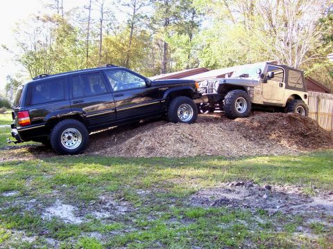 2004 Jeep TJ - Two Jeeps are positioned on a large pile of mulch in a grassy yard.