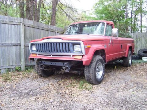2004 Jeep TJ - A red pickup truck is parked outdoors, with a wooden fence in the background and a missing front bumper.