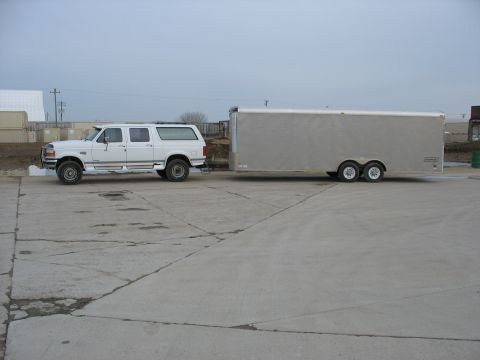 1995 Ford C-350 (Centurion Conversions) - A white Ford SUV tows a large silver trailer on a concrete lot under an overcast sky.