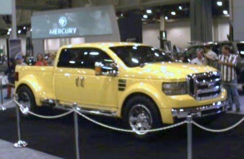 1981 Ford Bronco - A bright yellow pickup truck is showcased at an event, with people in the background.