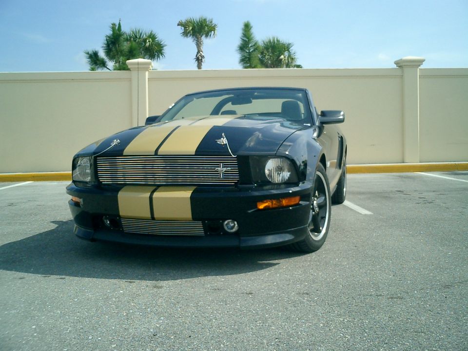 Black 2007 Ford Mustang convertible with gold racing stripes parked in a lot