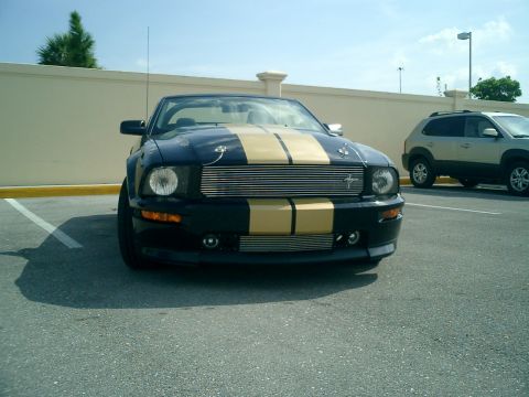 2007 Ford Mustang - A black Ford Mustang convertible with gold racing stripes is parked in a lot on a sunny day.