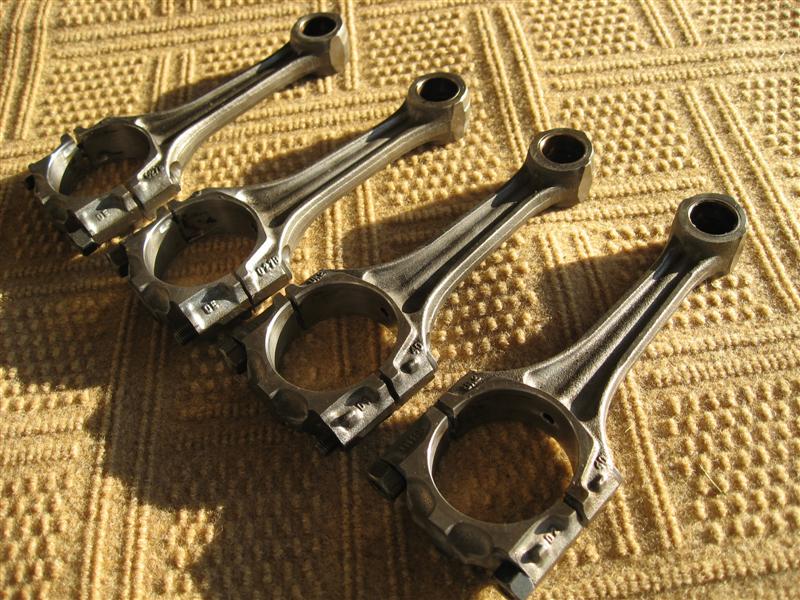 Four steel engine connecting rods with cap bolts laid on gold carpet