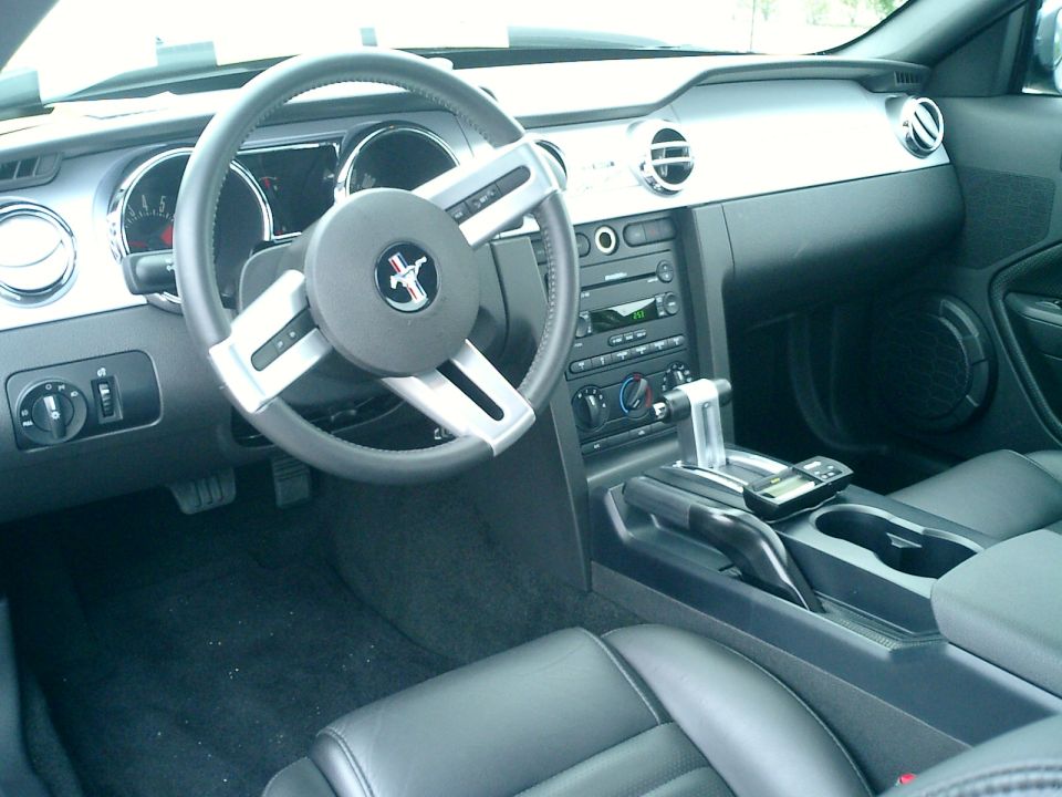 Car interior with steering wheel, dashboard, center console, and seats. Shows a Mustang logo on the steering wheel