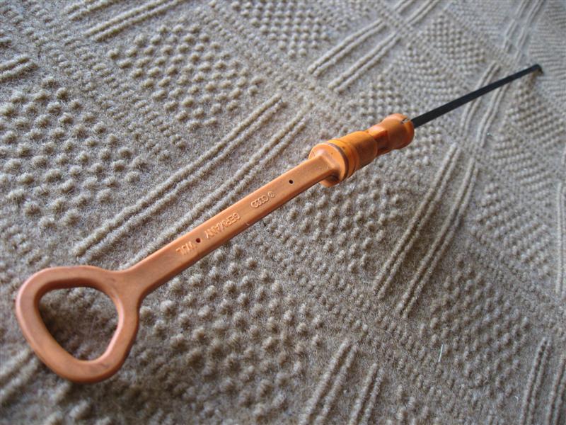 Orange Audi engine oil dipstick with triangular handle on a tan blanket