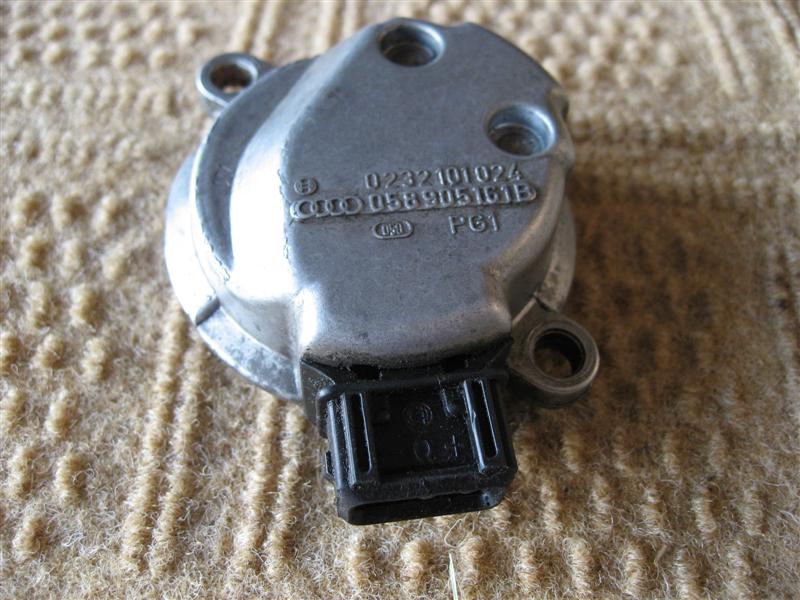 Aluminum automotive solenoid/sensor with black connector, marked 058 905 161 B, on carpet.