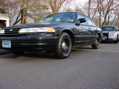 2003 Ford Crown Victoria - A black 2003 Ford Crown Victoria is parked on the street, with another Crown Victoria behind it.
