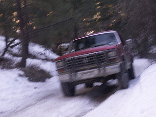 Red pickup truck driving on a snowy incline, front 3/4 view