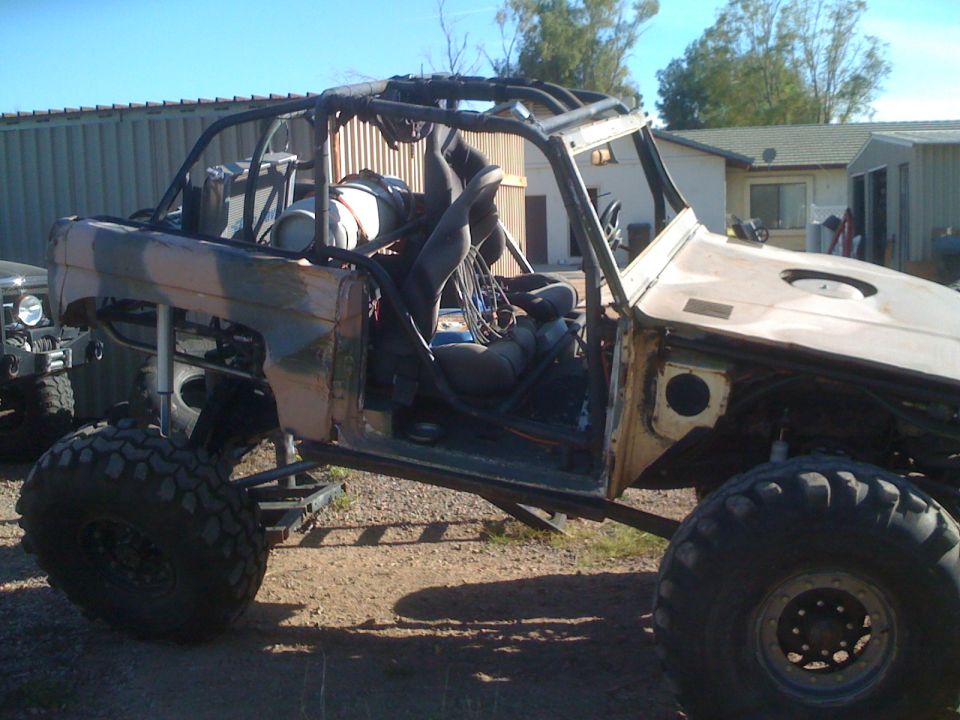 1966 Ford Bronco modified for off-roading, with roll cage and large tires. Another vehicle is partially visible to the left