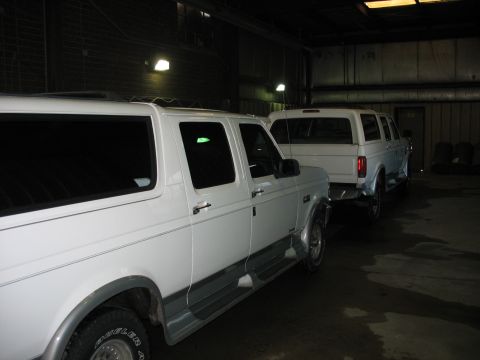 1995 Ford C-350 (Centurion Conversions) - Two white pickup trucks are parked side-by-side in a dimly lit garage.