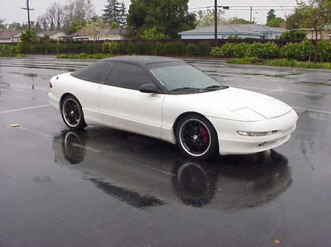 1994 Ford Probe - A white 1994 Ford Probe coupe with a black roof and tinted windows sits in a wet parking lot.