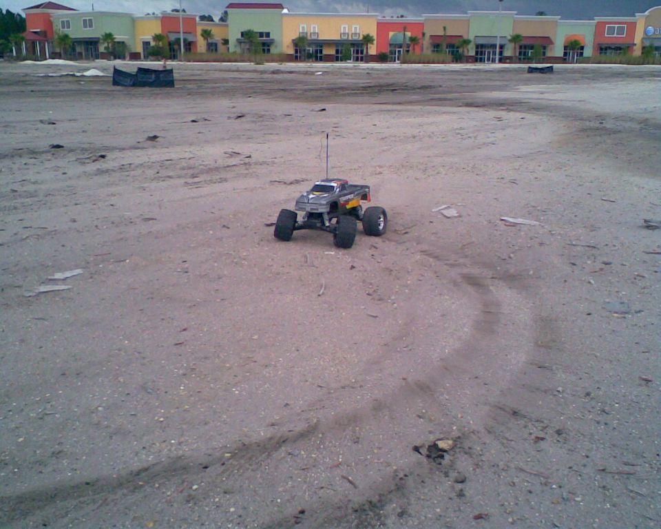 Remote control monster truck on sandy terrain with buildings in background