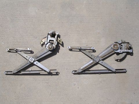 1983 Ferrari Enzo - Pair of car window regulators with electric motors shown on a concrete surface.